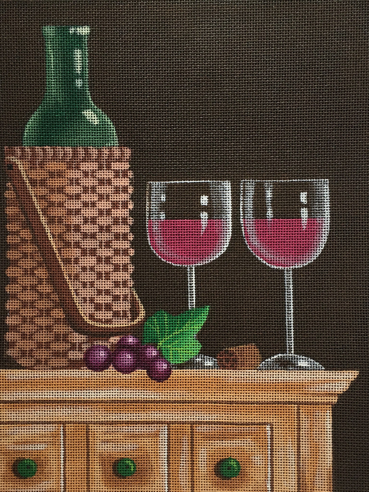 Kim Leo rustic needlepoint canvas of a bottle of wine and two glasses on a farmhouse chest with grapes