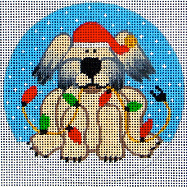 DC Designs round Christmas needlepoint canvas of a fluffy dog wearing a Santa hat holding Christmas lights in his mouth in the snow
