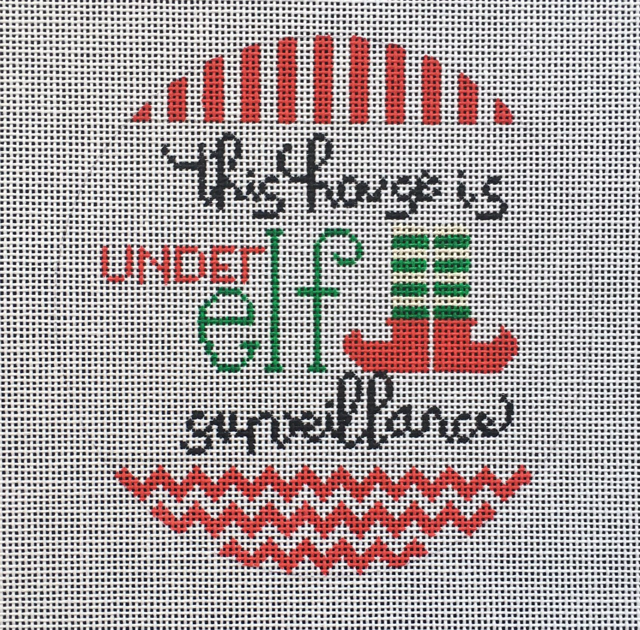 Vallerie Needlepoint Gallery round needlepoint canvas with the silly pun phrase "this house is under elf surveillance" with elf legs and red and white stripe and zig zag trim