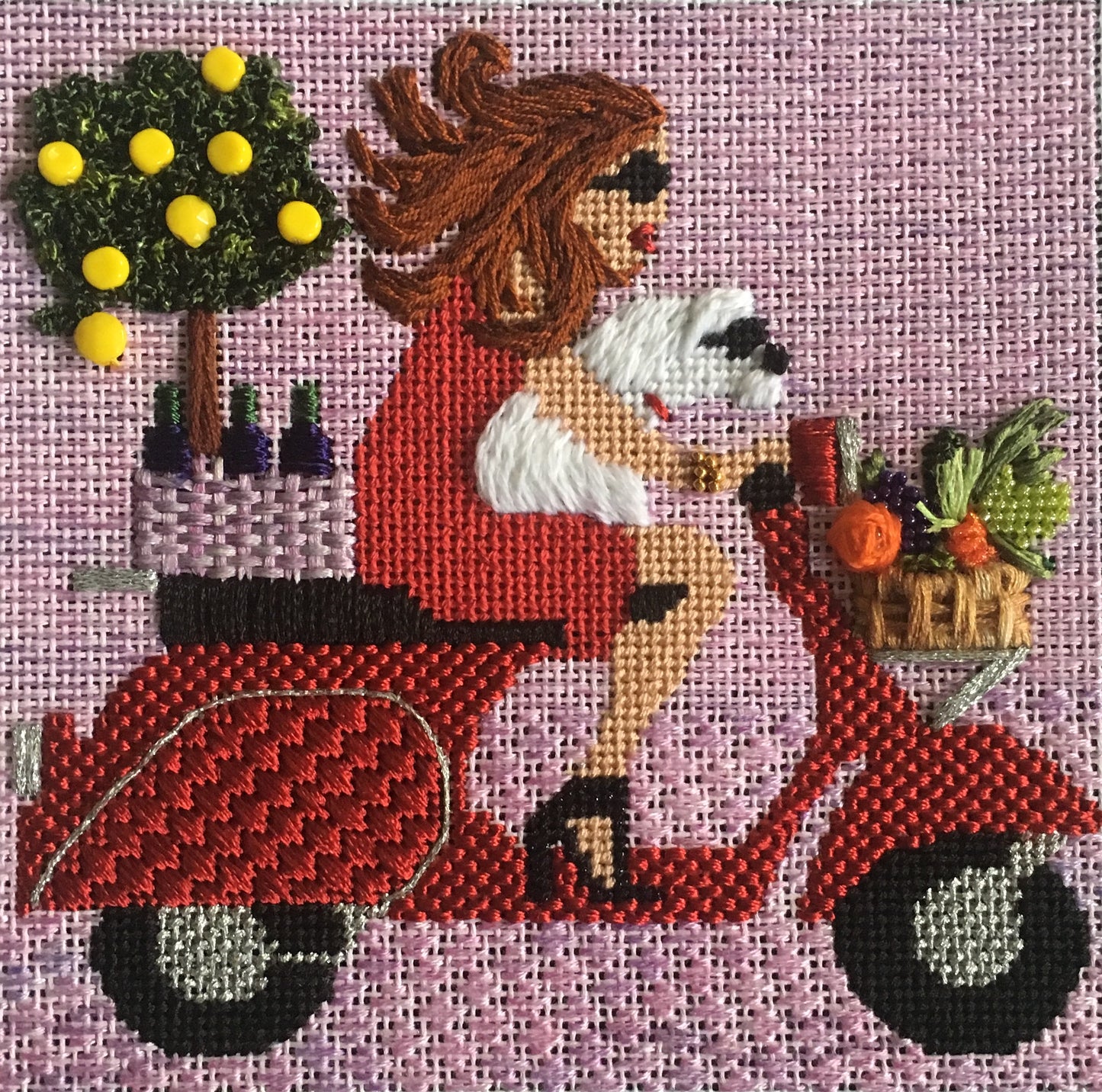 Stitched example of the Melissa Prince needlepoint canvas of a woman riding a Vespa motor scooter with a dog and wine and lemon trees in the background