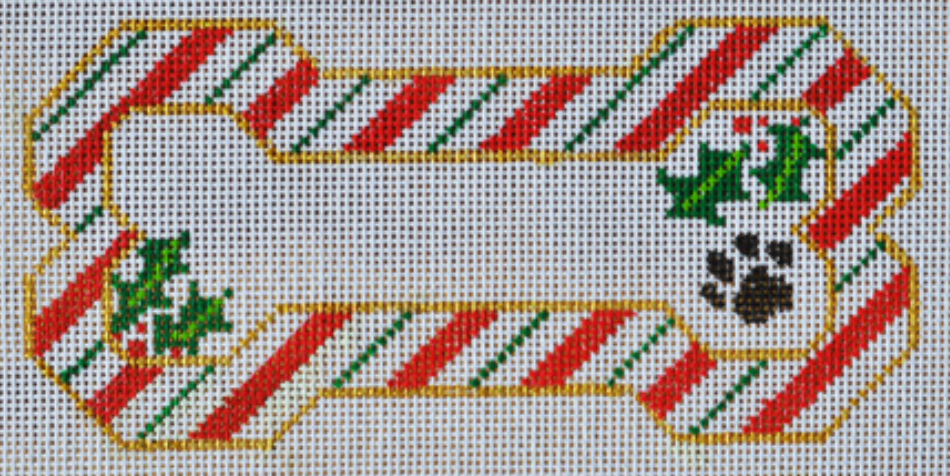 Danji Designs shaped needlepoint canvas of an ornament-sized dog bone with a candy cane striped border and a blank middle section for your dog's name. The ends have holly leaves and berries and there is a small black paw print in one corner