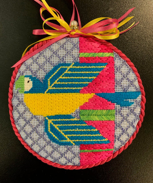 Scott Partridge round needlepoint canvas of a geometric and stylized tropical flying parrot in blue and yellow with a pink and purple background